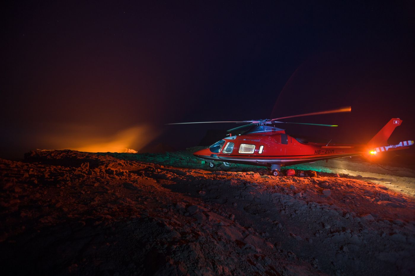Red helicopter at night beside a glowing lava lake