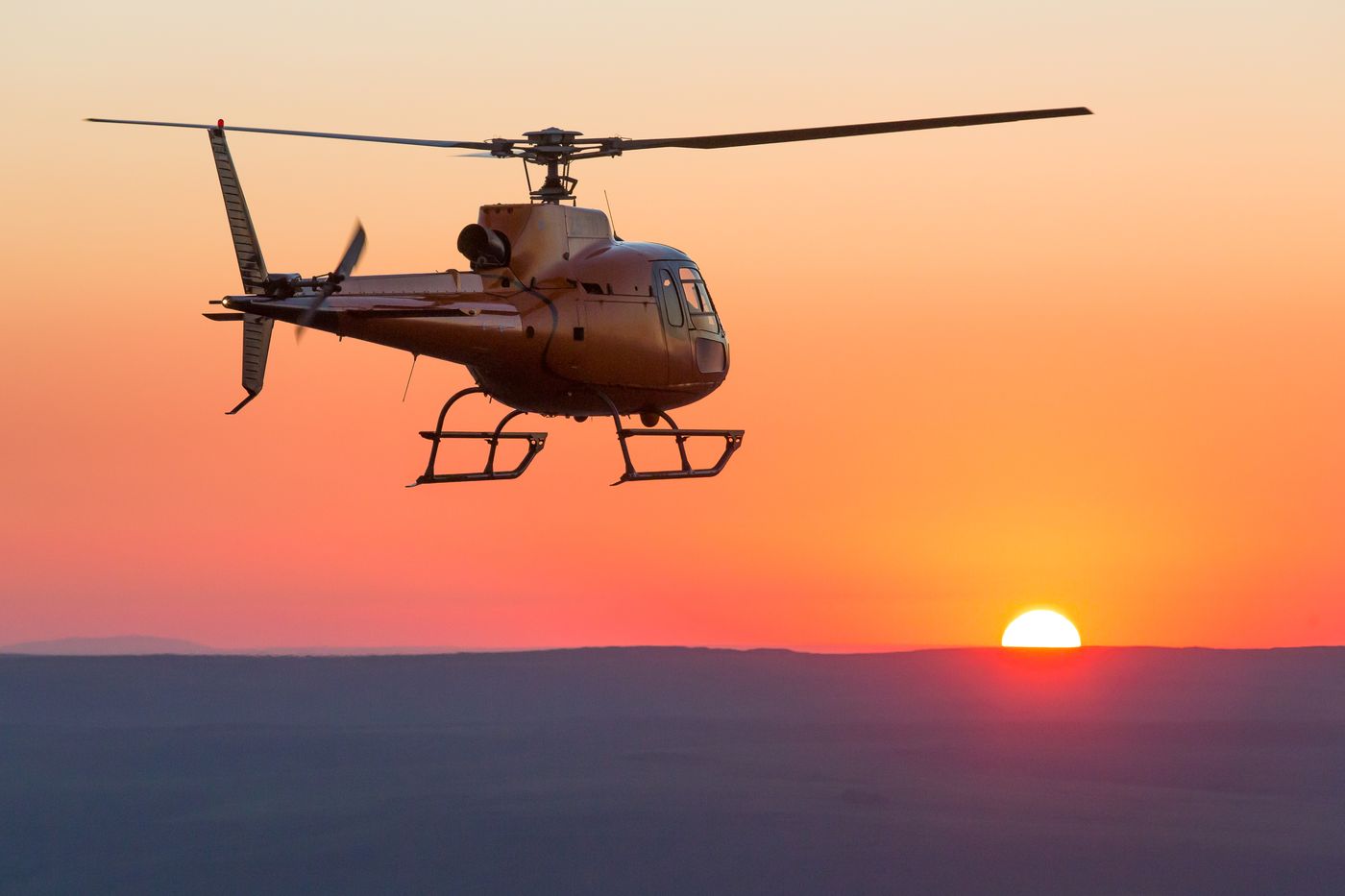 Helicopter flying across an orange sunset sky