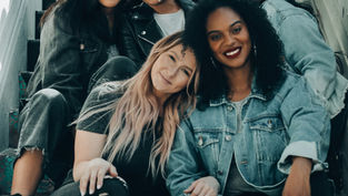 A portrait of a diverse group of women smiling while sitting together on a colourful staircase.
