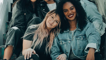 A portrait of a diverse group of women smiling while sitting together on a colourful staircase.