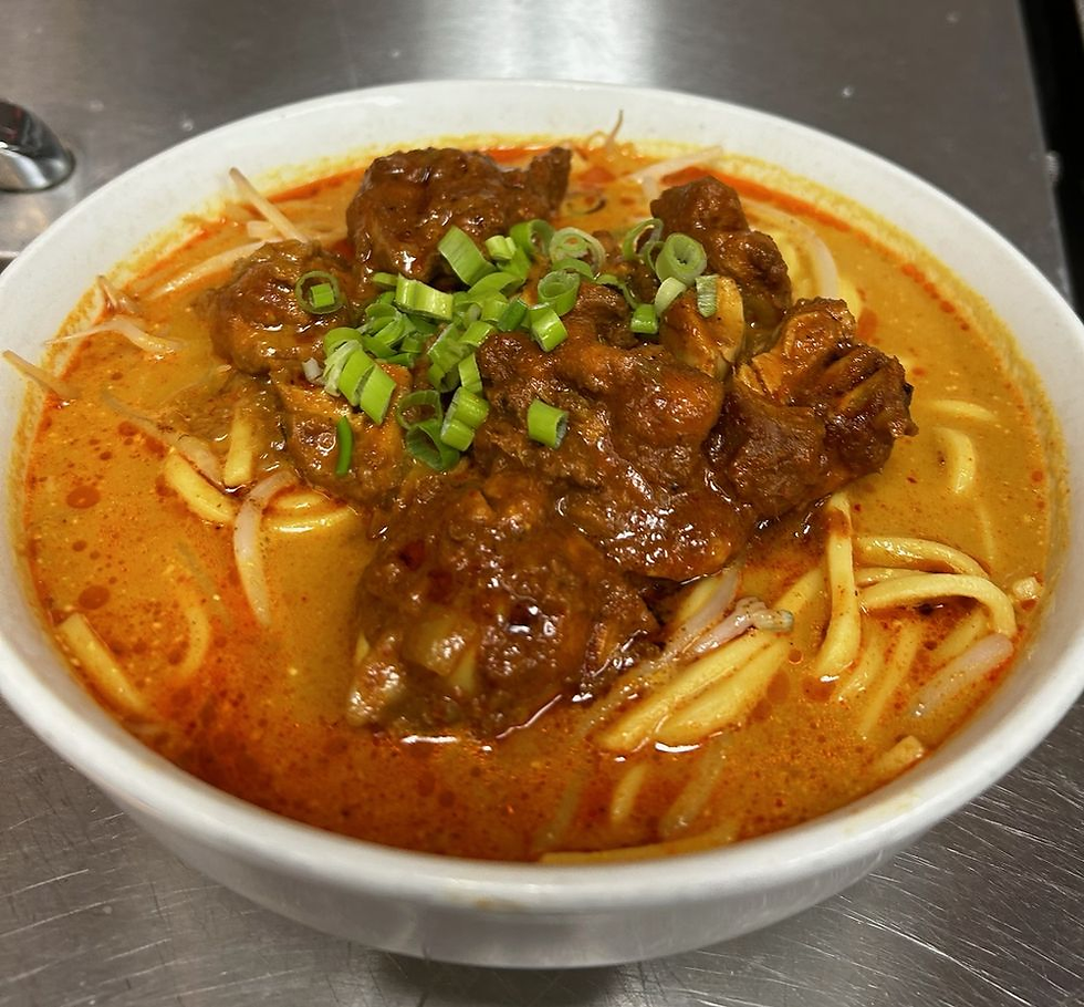 A bowl of spicy noodle soup with chunks of meat, topped with chopped green onions. The soup has a rich, red broth.