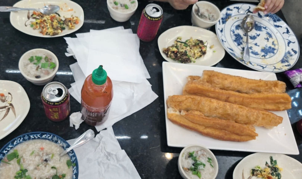 A table with congee bowls, fried dough sticks, and cans. A person is eating. Sriracha bottle and napkins are on a black surface.