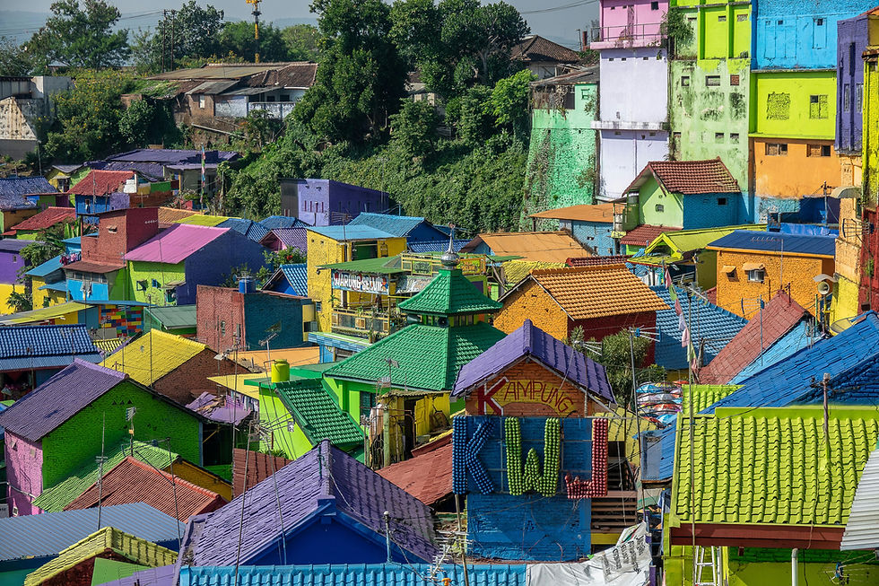 Colorful houses in a vibrant village with green hills in the background. Roofs are painted in bright hues; signs read "Warung Semeti" and "Kampung."