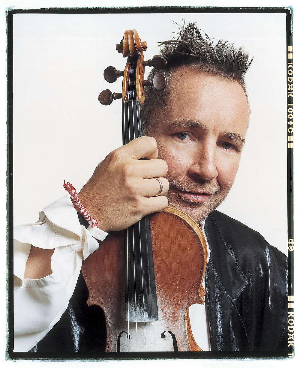 Nigel Kennedy holding his violin and smiling into the camera
