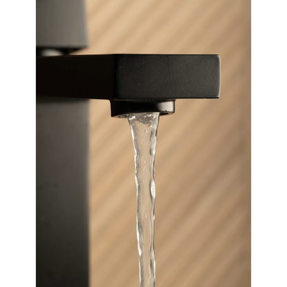 Close-up of water flowing from a sleek matte black faucet, with a wood-toned textured wall in the background.