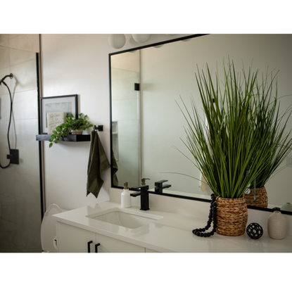 Modern bathroom with a large mirror, black fixtures, white countertop, and decorative accents including a woven plant basket and black bead strand.