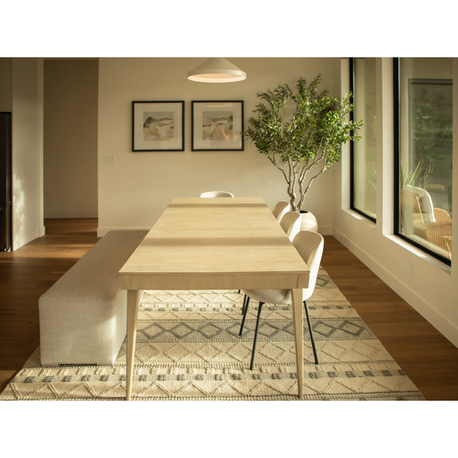 The dining room embraces organic minimalism with light wood finishes, floor-to-ceiling windows, and a cozy built-in bench. A potted tree brings nature indoors, completing the scene.
