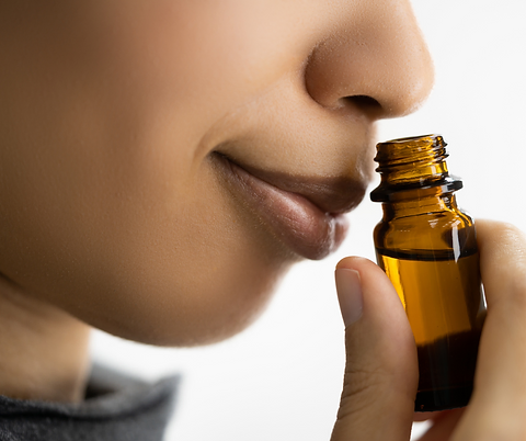 A smiling person smelling essential oils from a bottle.