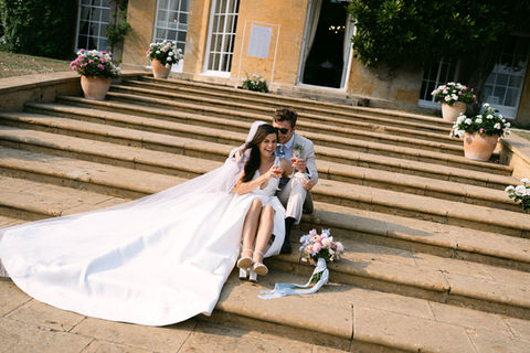 Bride and groom sitting on stone steps laughing during wedding reception at North Cadbury Court