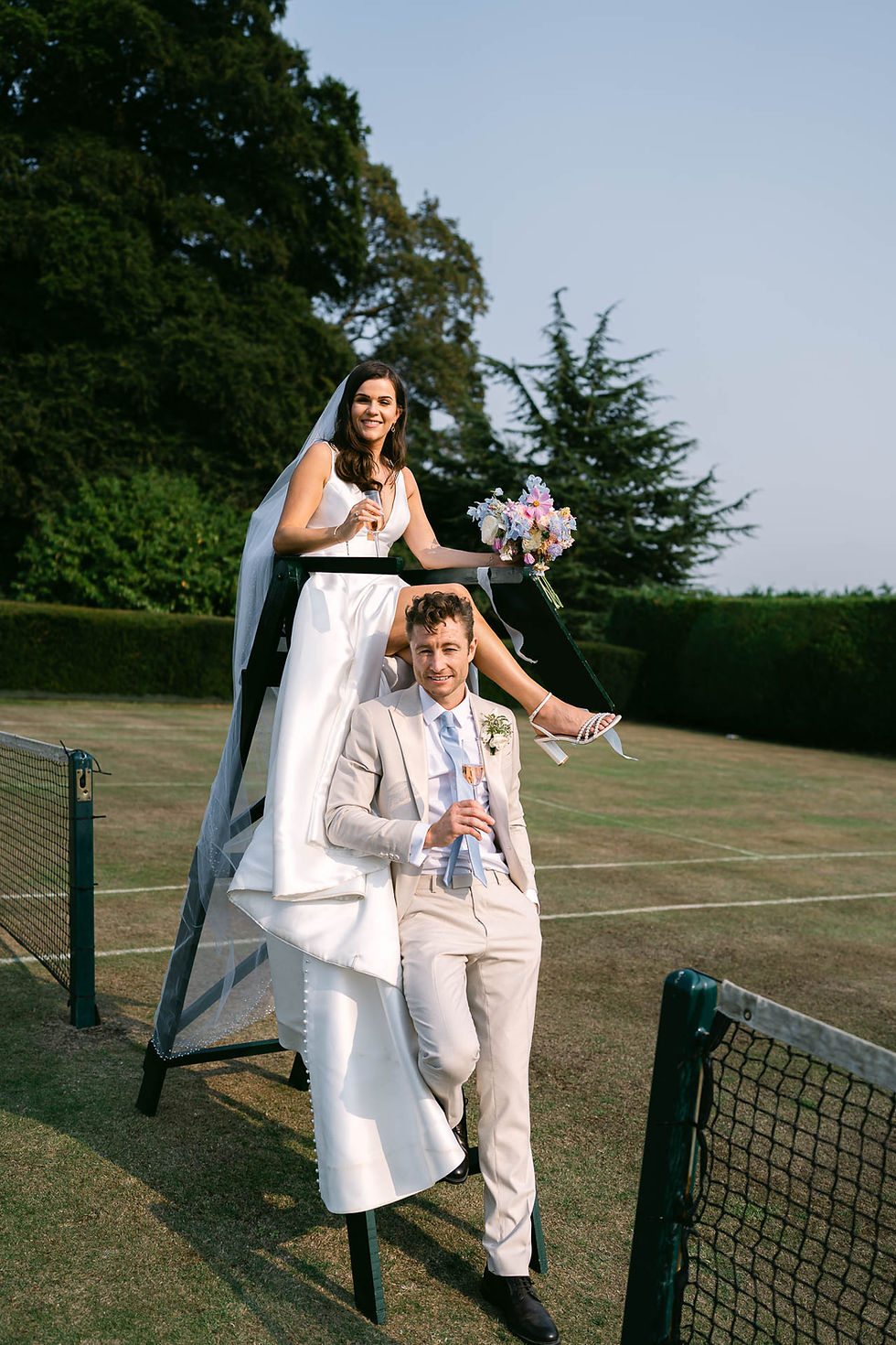 Bride and groom posing playfully on tennis court at North Cadbury Court wedding in Somerset, natural documentary wedding photography