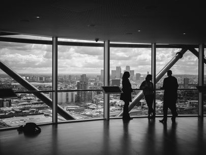 : Black-and-white photo of professionals standing together in a tall office building with floor-to-ceiling windows overlooking a city skyline, symbolizing teamwork, growth, and embracing new perspectives in sales culture.