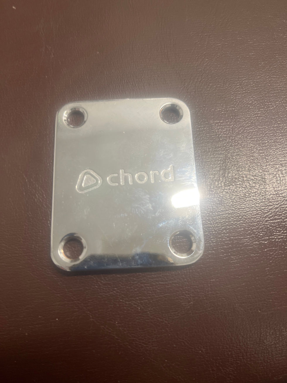Chrome guitar neck plate with the word chord and four mounting holes.