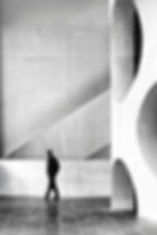 Homme marchant dans un couloir moderne noir et blanc, devant un mur géométrique à arches circulaires.