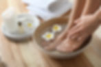 Closeup view of woman soaking her feet in dish with water and flowers on wooden floor. Spa