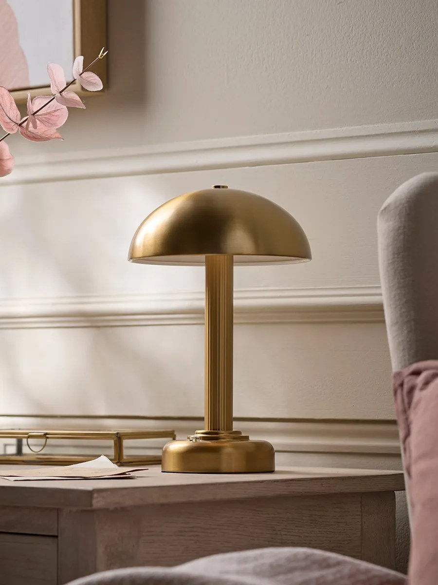Small brass-toned rechargeable table lamp with a mushroom-style shade glowing on a side table