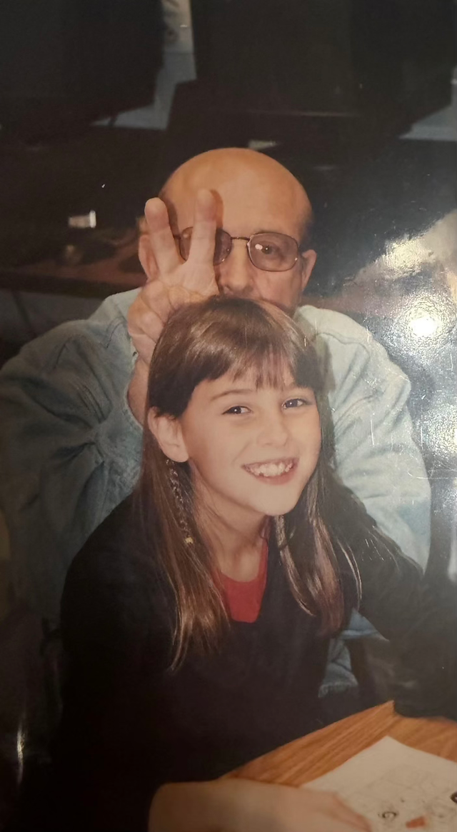Portrait of Kim Needham, LPC of Visions Counseling & Education seen posing for a photo with her grandfather. He is giving her 'bunny ears' with his fingers behind her back.