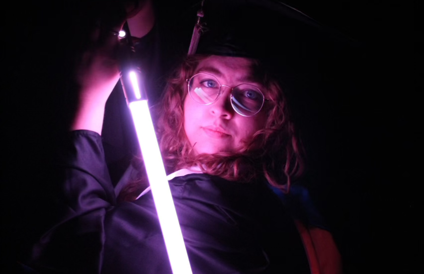 Portrait of Bryn Winegar, LPC at Visions Counseling & Education in Boise posing in the dark while holding a lightsaber that illuminates her face.