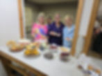 Four people smiling behind a spread of food