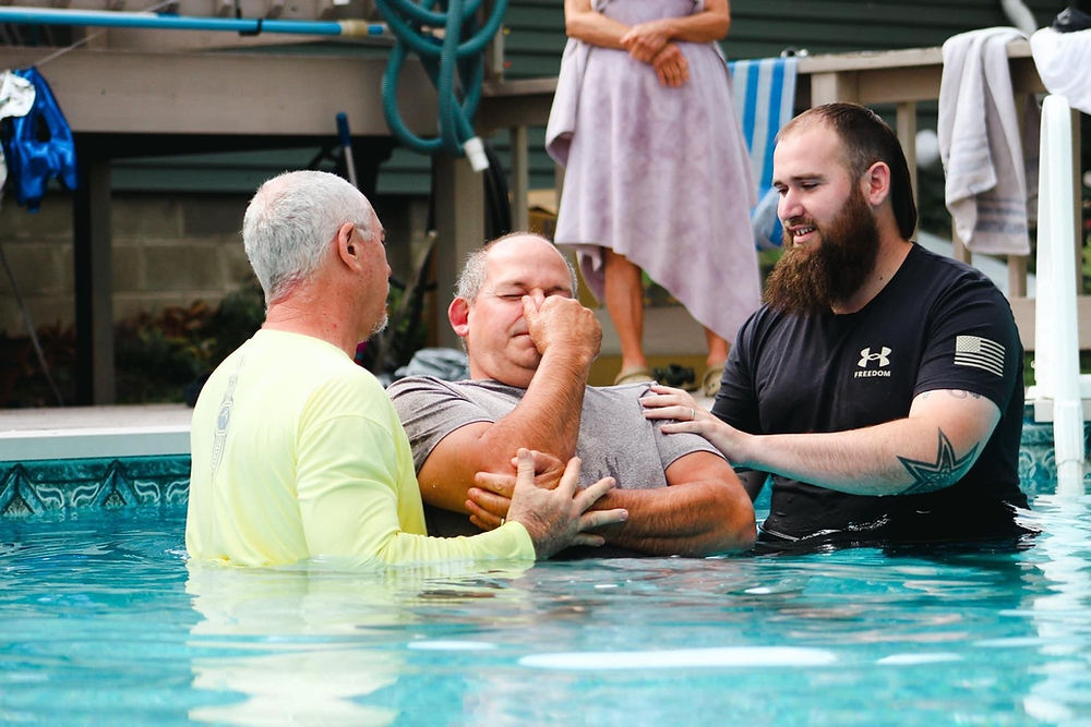 Emotional man being baptized in a pool by two men
