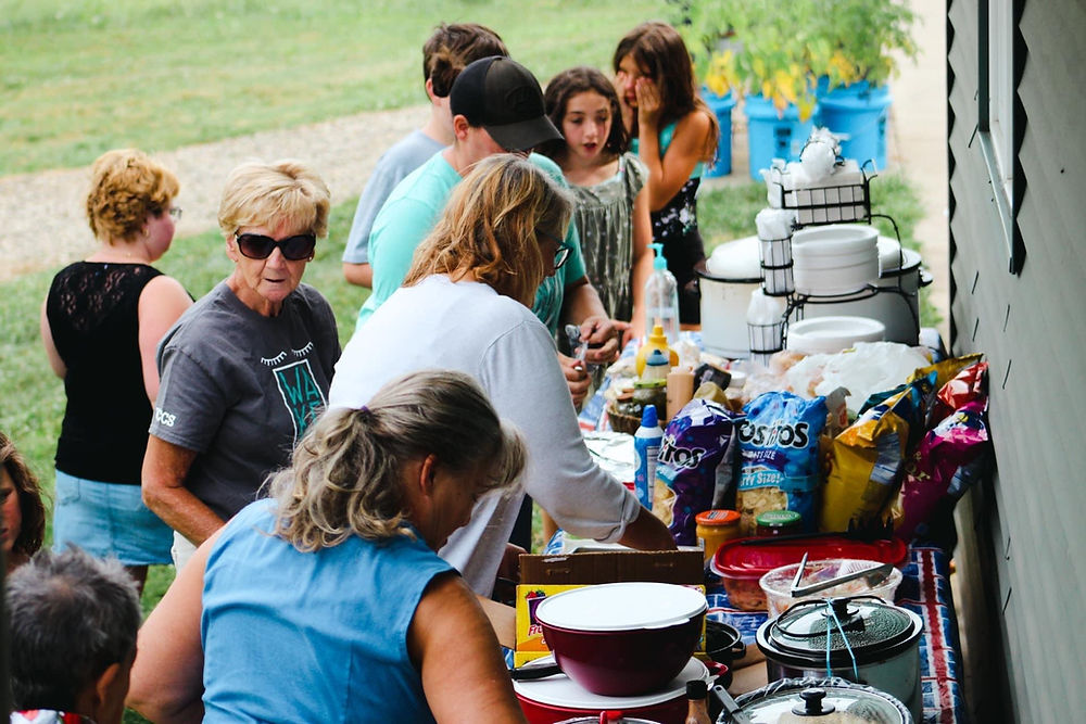 People gather around a table with food and snacks outdoors