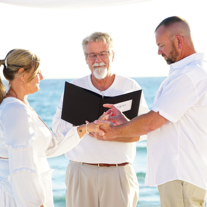 Couple exchanging rings under wedding arch on the beach