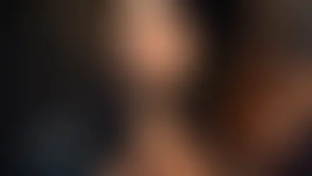 Porträt einer Frau im warmen Sonnenlicht, die eine sehr filigrane, goldfarbene Halskette mit floralen Details und einen kleinen Ohrstecker trägt. Ein dunkler, locker über die Schulter fallender Blazer unterstreicht das unbeschwerte, luftige Sommer-Styling.