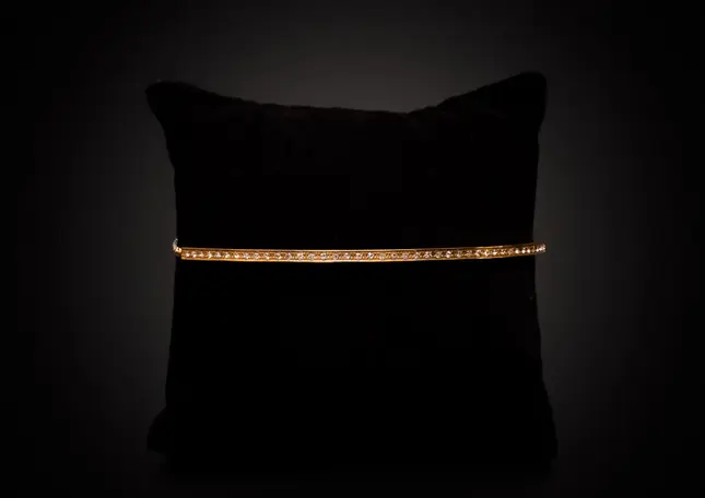 Goldfarbenes Armband mit feinen Kristallen, frontal auf schwarzem Kissen präsentiert.