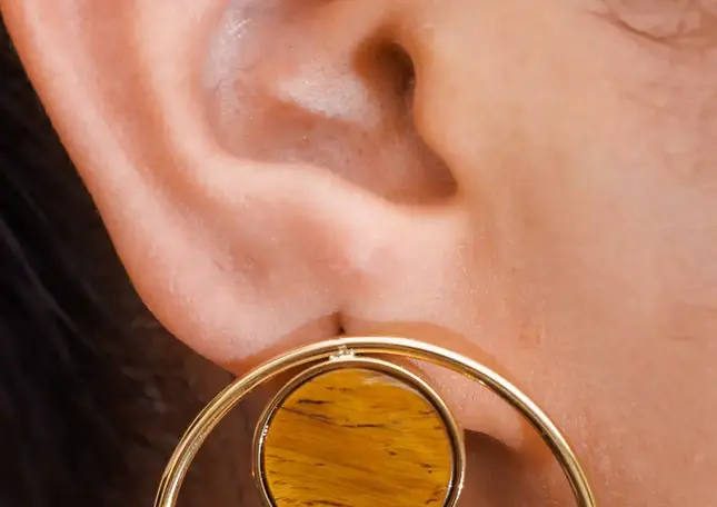 Ohrringe goldfarben mit Naturstein – getragen am Ohr, goldener Kreisrahmen mit sichtbarem Naturstein.