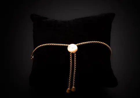 Rückseite des goldfarbenen Armbands mit verstellbarem Kugelverschluss auf dunklem Untergrund.