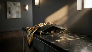 Zwei goldfarbene Ketten auf Konsole neben Clutch und Seidentuch im Abendlicht – Layering ohne Chaos, Avirelle.