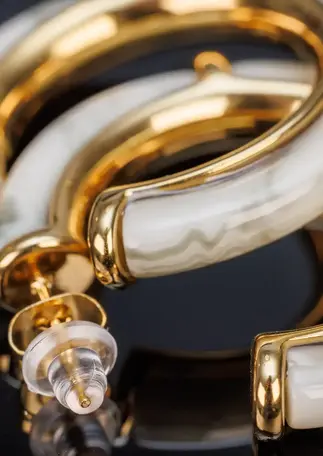 Detailaufnahme der Creolen goldfarben mit Acetat, Fokus auf Verschluss und Materialstruktur.