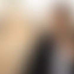 Frau im Blazer trägt silberfarbene Kette mit goldfarbenem Zentrum vor unscharfer Stadtkulisse, Avirelle.