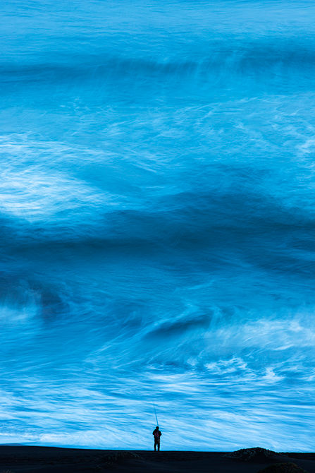 Man sea fishing from the beach with the sea as a wall in front of him at Matanzas in Chile