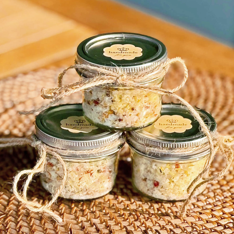 Three small jars filled with a colorful mixture, topped with green lids labeled "handmade." Jars are tied with twine and stacked on a woven mat.