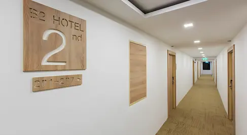 Guest corridor at B2 Ubon Premier Hotel featuring timber doors, clear wayfinding signage, and recessed lighting.
