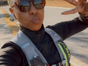 Woman walking outdoors on a neighborhood road, wearing sunglasses and a hydration vest, sharing her postpartum walking routine and fitness journey
