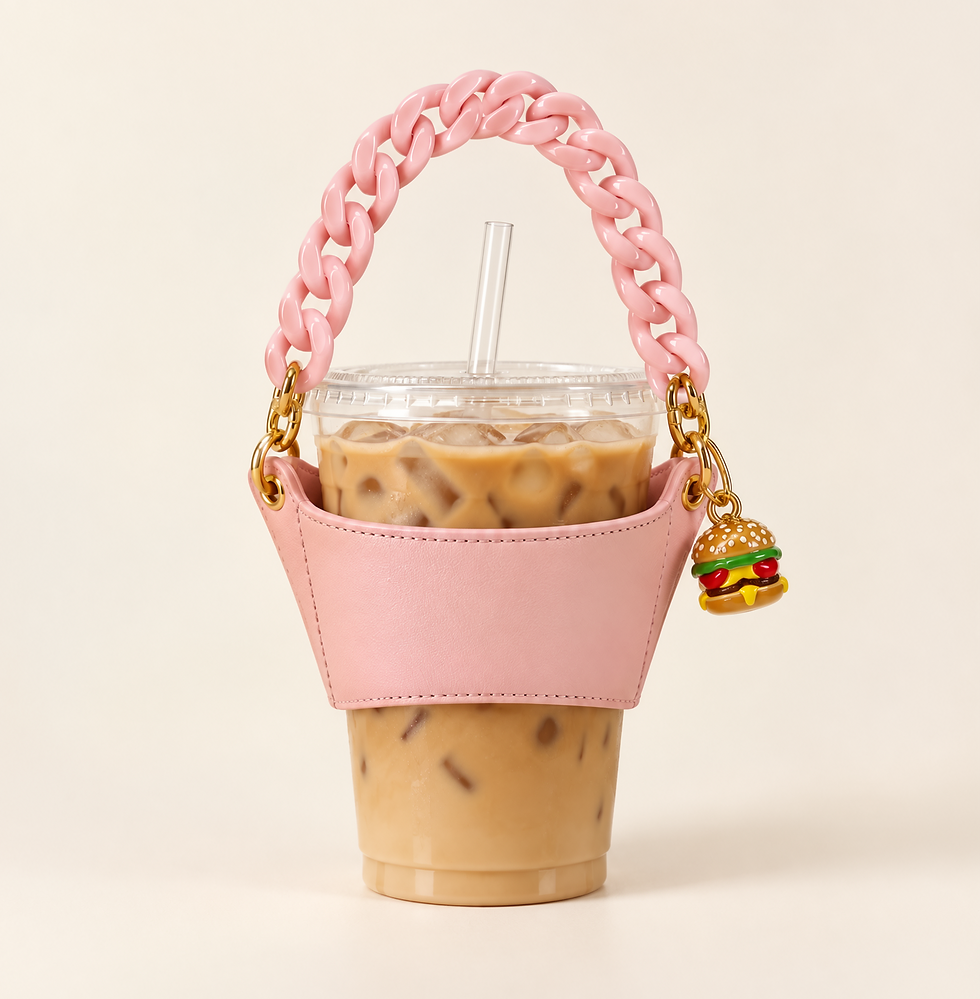 Studio photography of an iced coffee held in a pink leather-style cup carrier with a chunky pink chain handle and a burger charm. The aesthetic is cute, playful, and trendy.