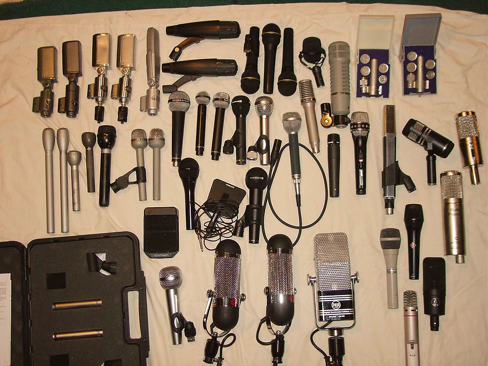 A collection of various microphones arranged on a cream cloth. Includes vintage and modern designs in silver, black, and metallic colors.