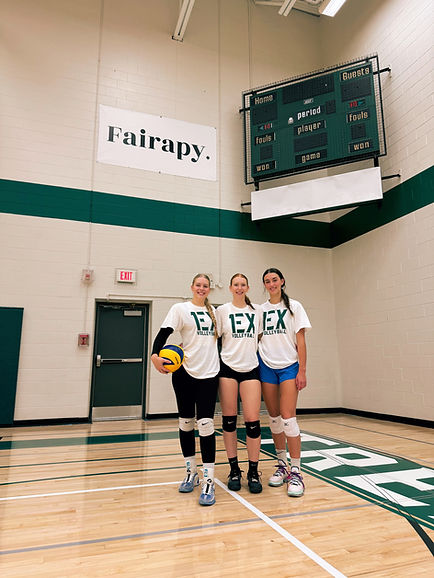 A photo of three post-secondary student athletes, smiling in their gym in front of the school's Fairapy banner