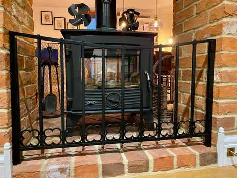 hand forged fire guard in a brick fireplace with a black wood burner 