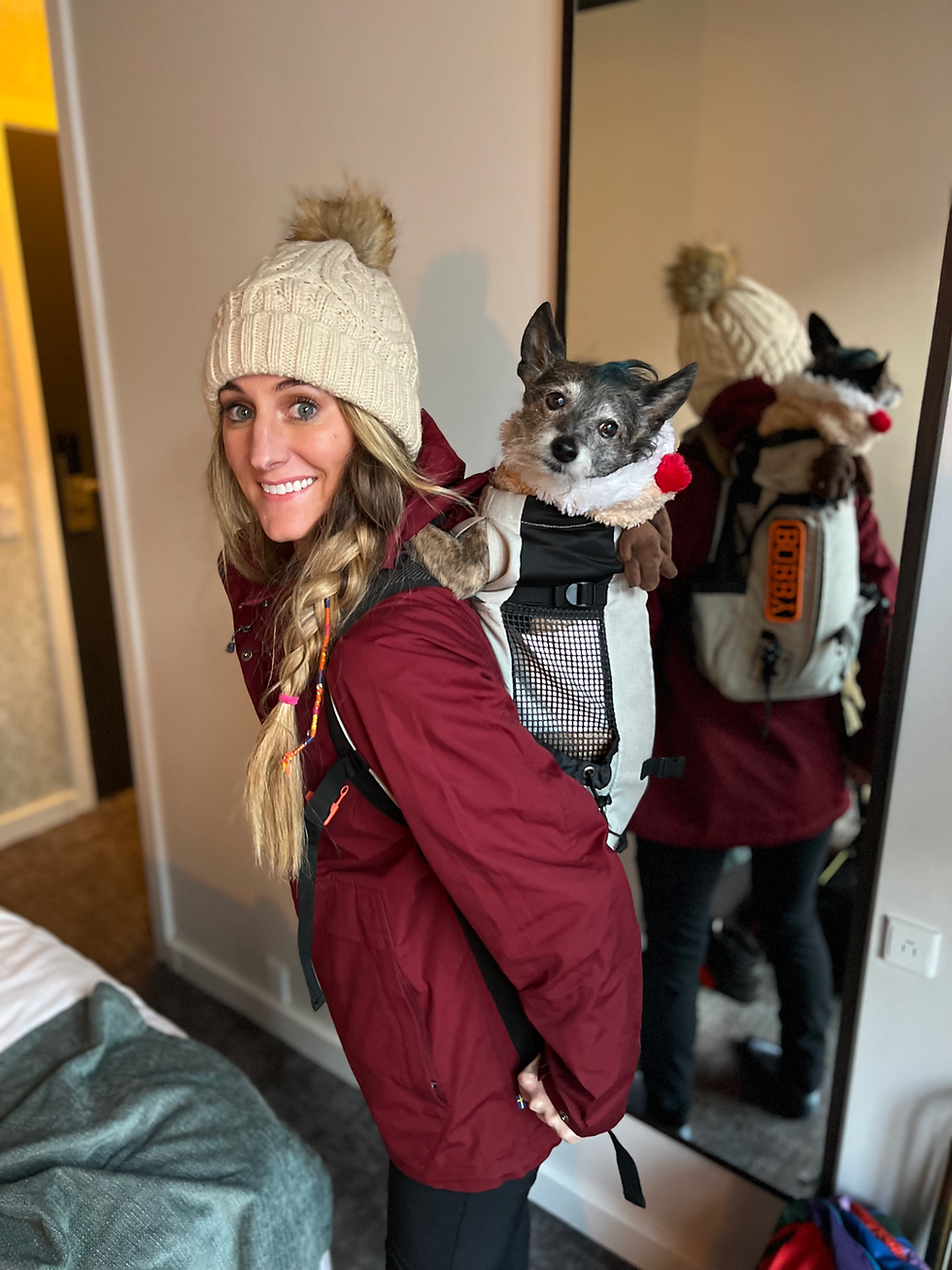 Smiling woman carrying a dog in a backpack carrier.