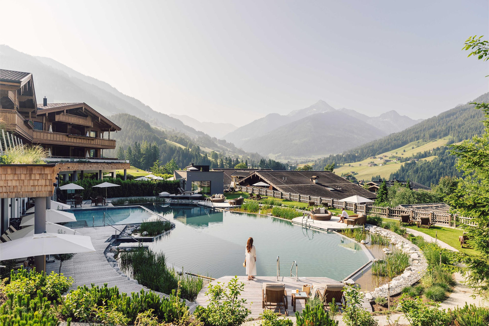 A girl walking around the outdoor pool with views of the alps at Hotel Boglerhof
