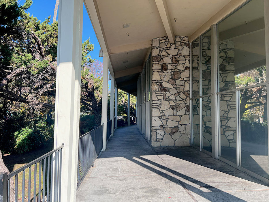 A cement walking path along the left-hand side of the Pleasant Hill campus building, with a white awning shading its route and white beams holding up the awning.