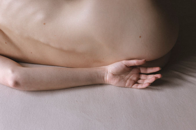 Rücken und Hand eines nackten Menschen auf dem Bett