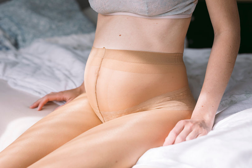 schwangerer Bauch im Sonnenlicht, sitzend auf dem Bett