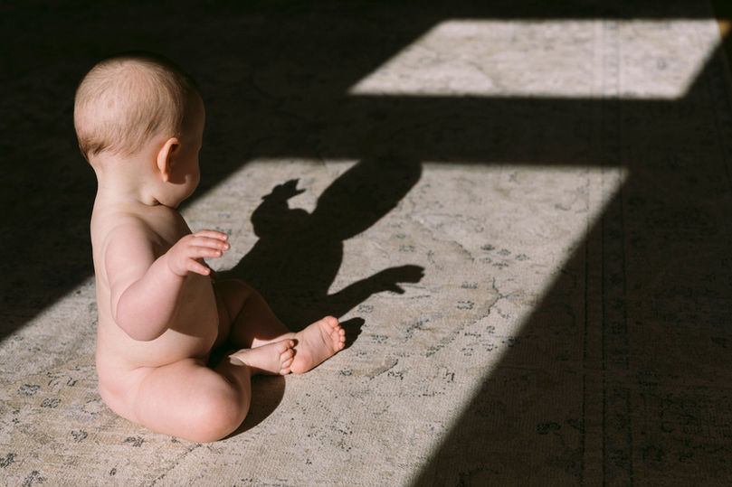 Kleinkind sitzt auf Teppich und spielt mit dem eigenen Schatten