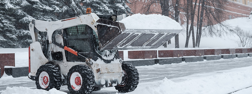 A small loader excavator bobcat removes snow from the sidewalk near the Kremlin walls duri