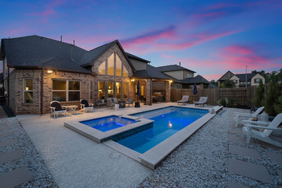 Beautiful twilight photo of a brick house featuring warm interior lighting, a glowing backyard pool, and a vibrant sunset sky that enhances the property’s inviting ambiance. Perfect example of professional twilight real estate photography. Captured by Strata Visuals.