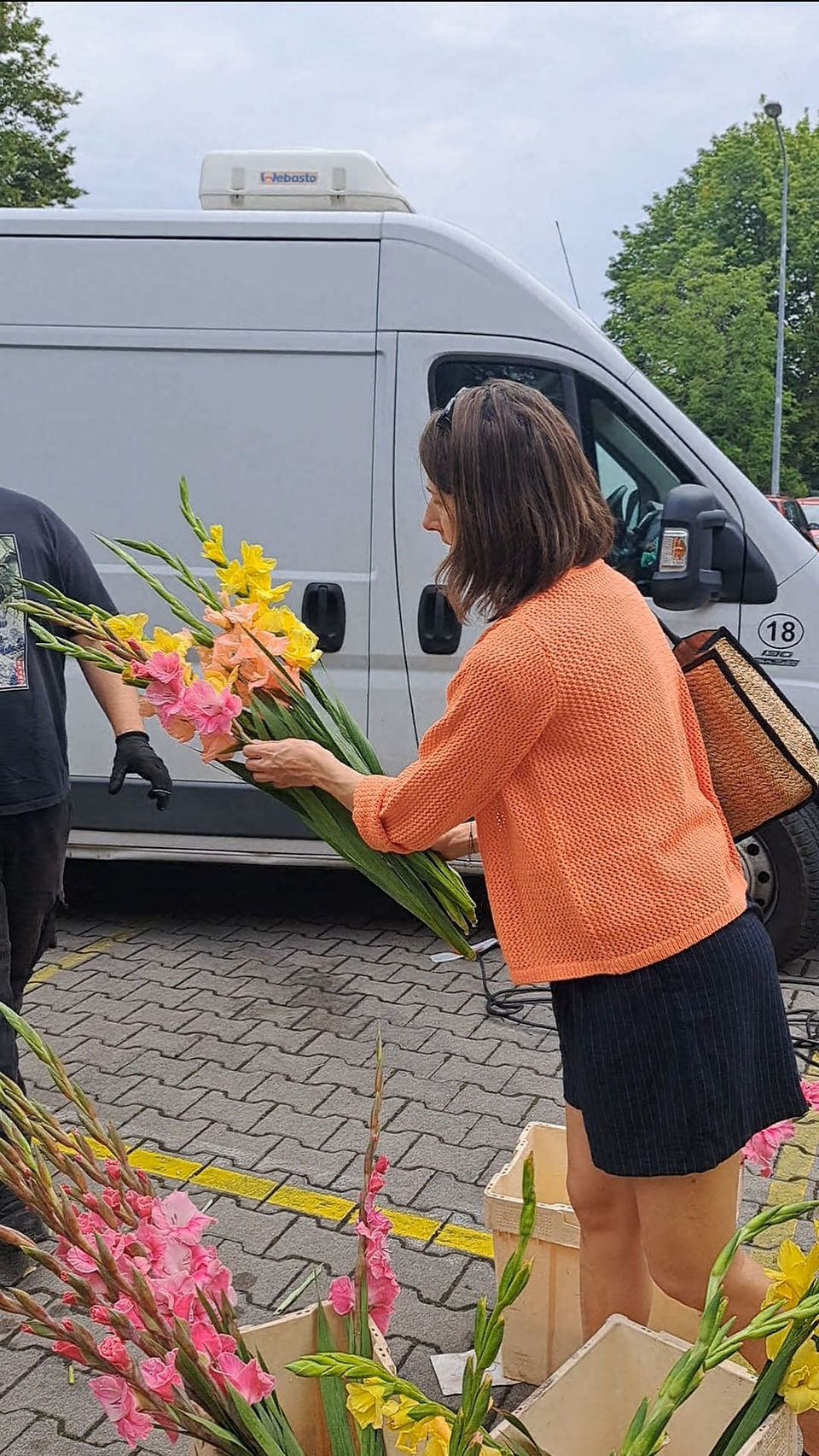 dziewczyna w pomarańczowym sweterku trzyma kolorowe gladiole, na rynku