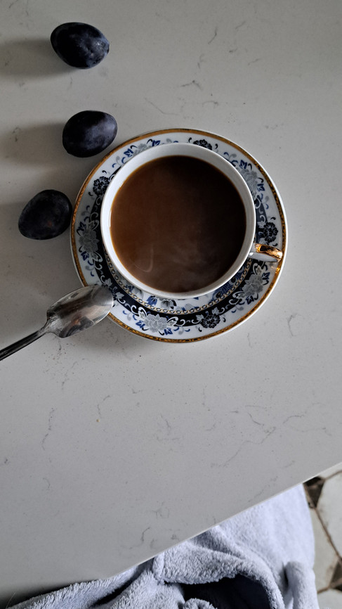 kawa w porcelanowej niebieskiej filiżance i śliwki na marmurowym blacie